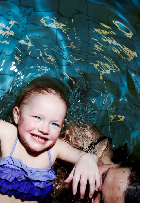 A smiling girl swimming in a pool with another woman