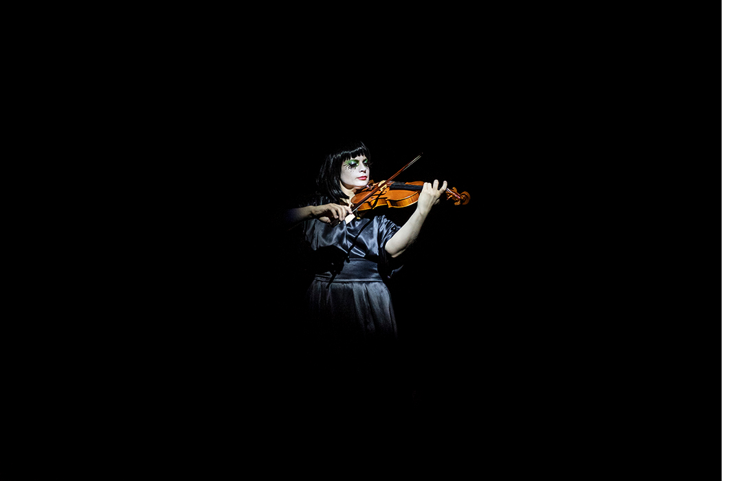 A girl illuminated by light plays the violin against a black background