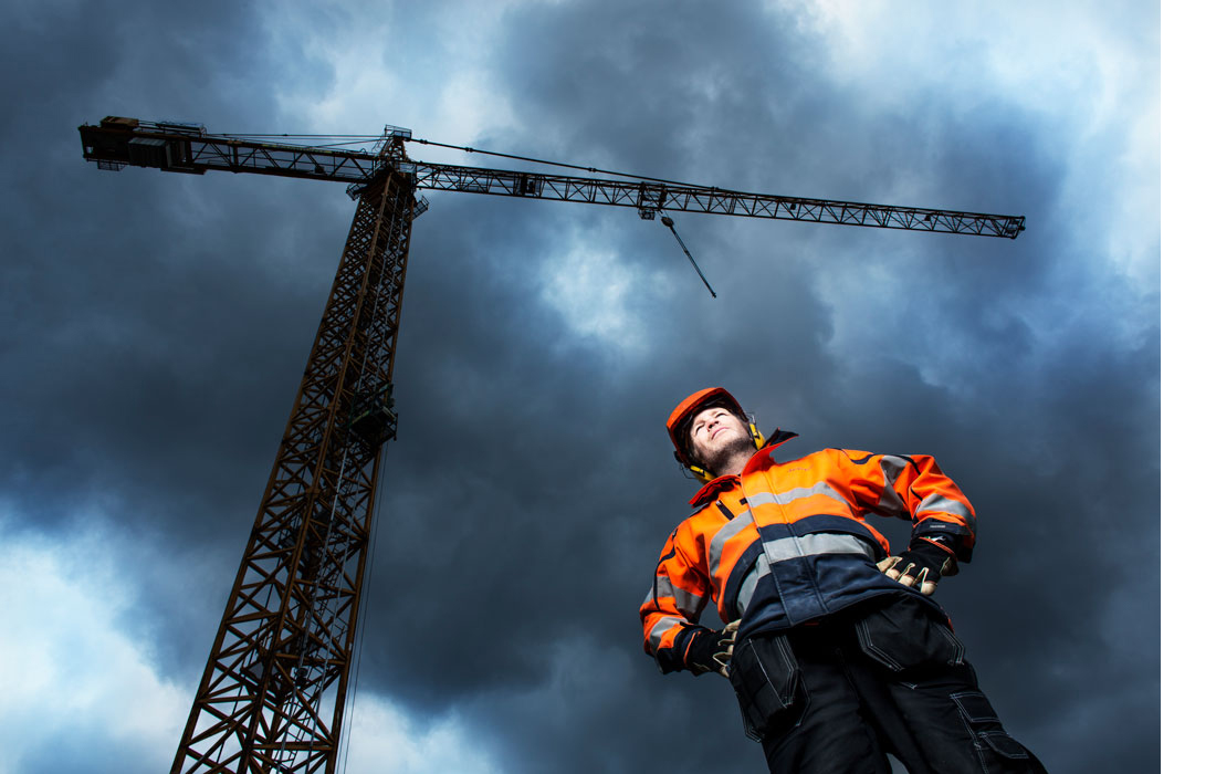 A construction worker is standing by a large crane