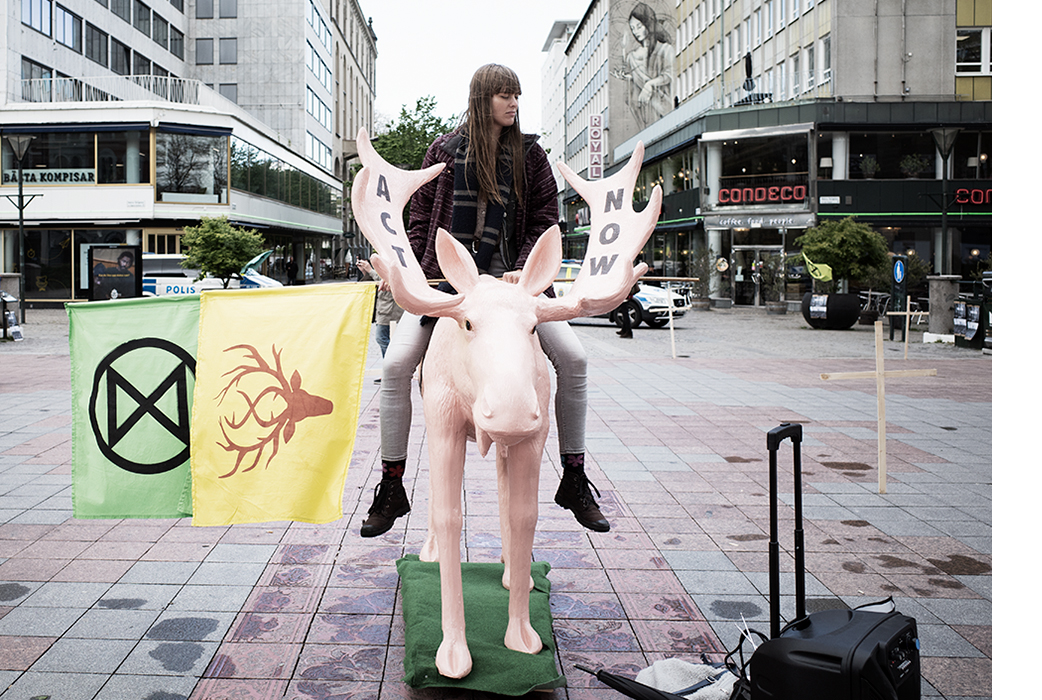 En ung kvinna sitter på en rosa älg skulptur i Malmö