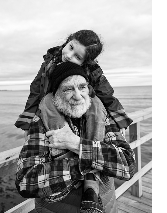 A grandfather has a girl on his shoulders on a dock by the sea