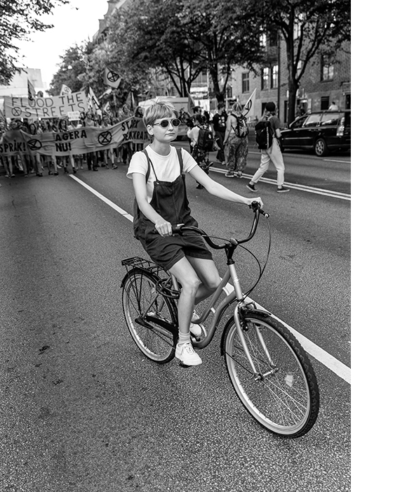 En pojke på en cykel med demonstrationståg i bakgrunden